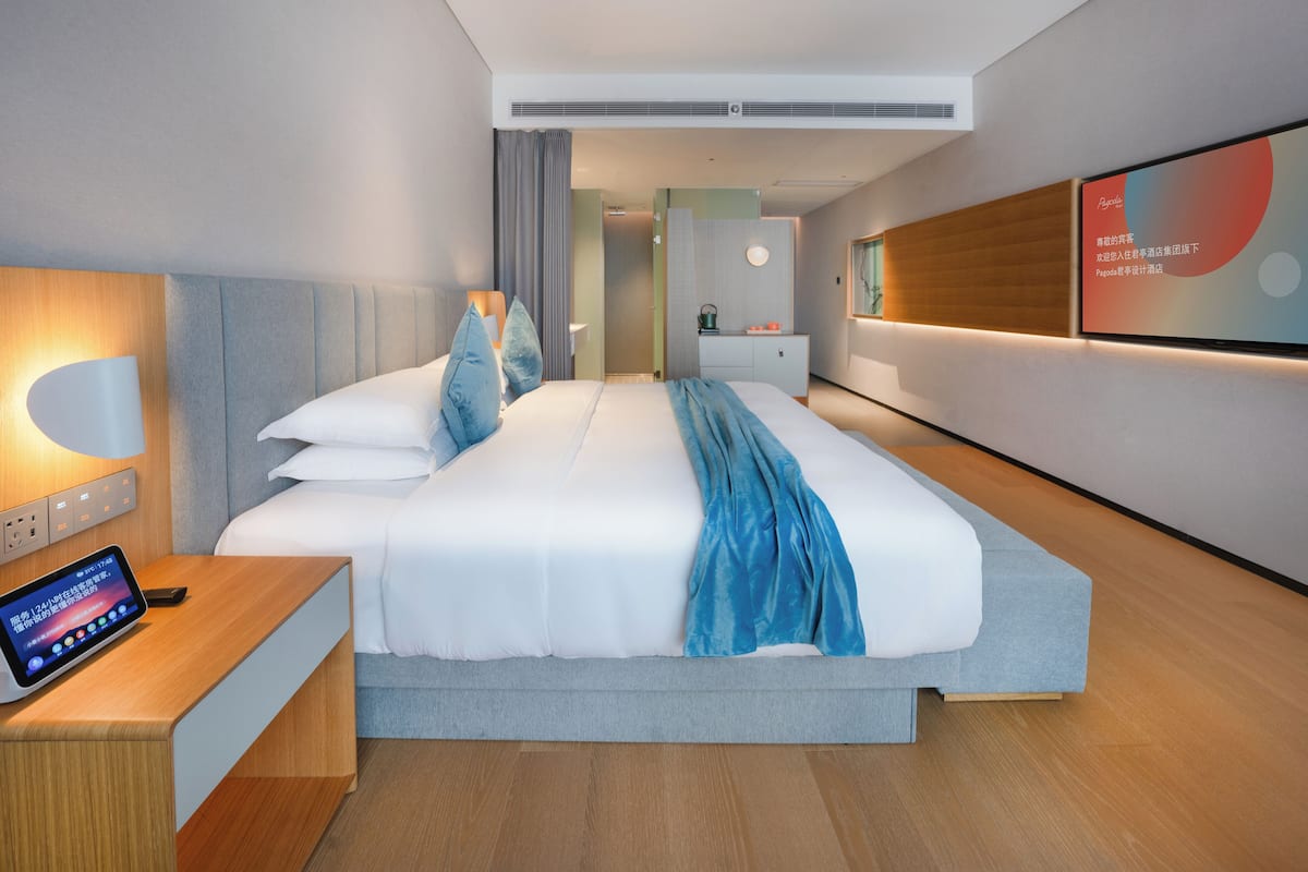 Una habitación de hotel moderna con una cama grande, una mesita de noche y un dispositivo digital que muestra información.