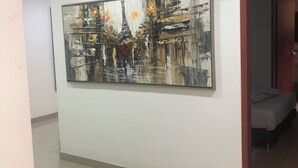 En hall med en stor, abstrakt målning av Eiffeltornet och blommor på väggen, en dörr med ett nummerskylt och en säng i det intilliggande rummet.