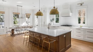 Une cuisine spacieuse dotée d’un grand îlot central, de meubles blancs et de luminaires suspendus.