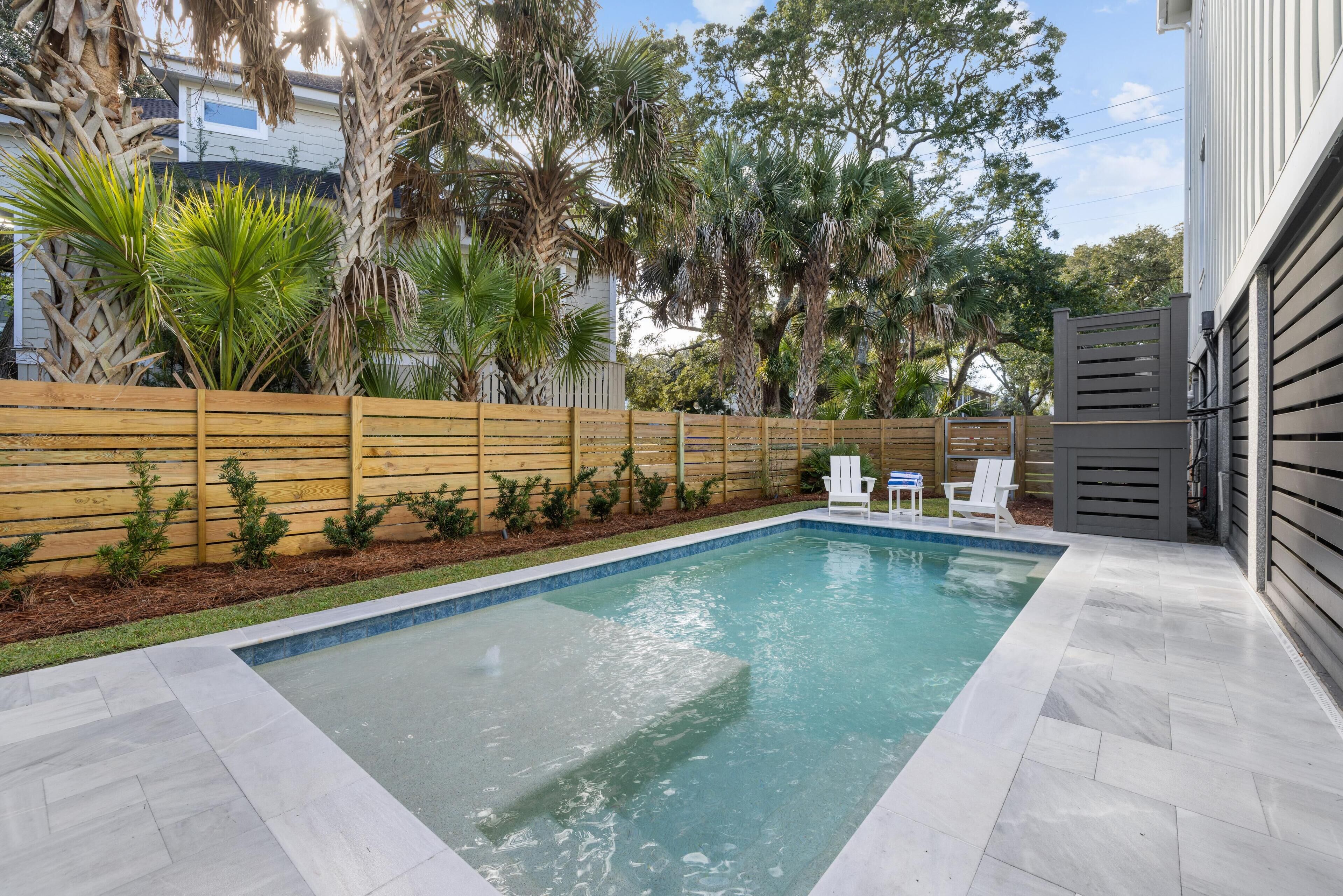 Piscina rectangular con valla de madera y plantas pequeñas, rodeada por un patio empedrado.