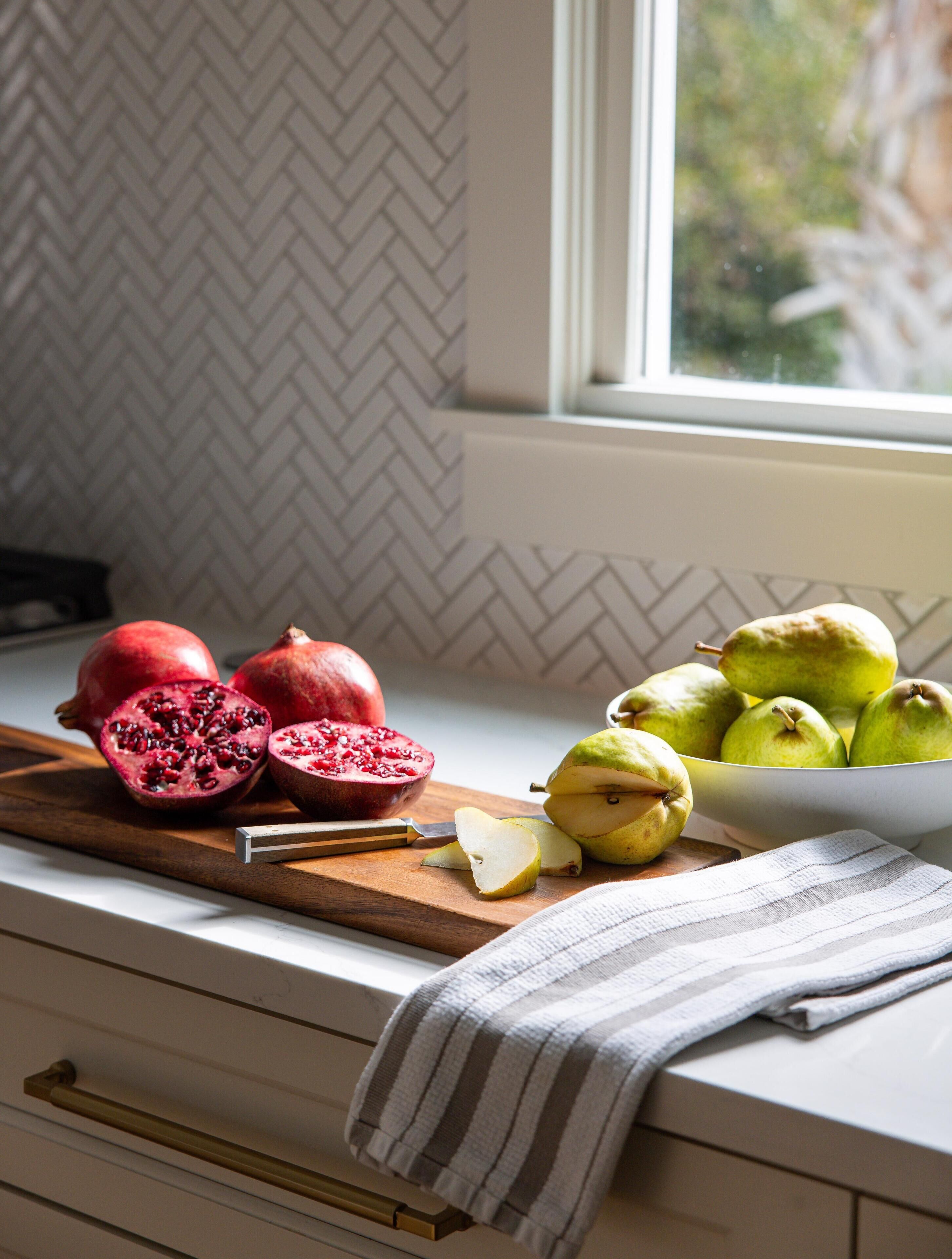 A kitchen counter with a cutting board, a bowl of pears, and a pomegranate cut in half.