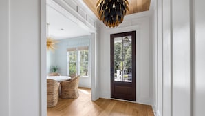 Un couloir doté d’un plancher en bois, d’une porte en bois sombre et d’un luminaire suspendu.