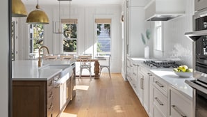 Une cuisine moderne avec des meubles blancs, un îlot central, des luminaires suspendus et une vue sur l’extérieur.
