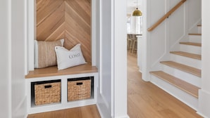 Un couloir avec un banc en bois disposé en motif chevrons, des paniers en osier et un escalier avec des marches en bois et une rampe en bois.