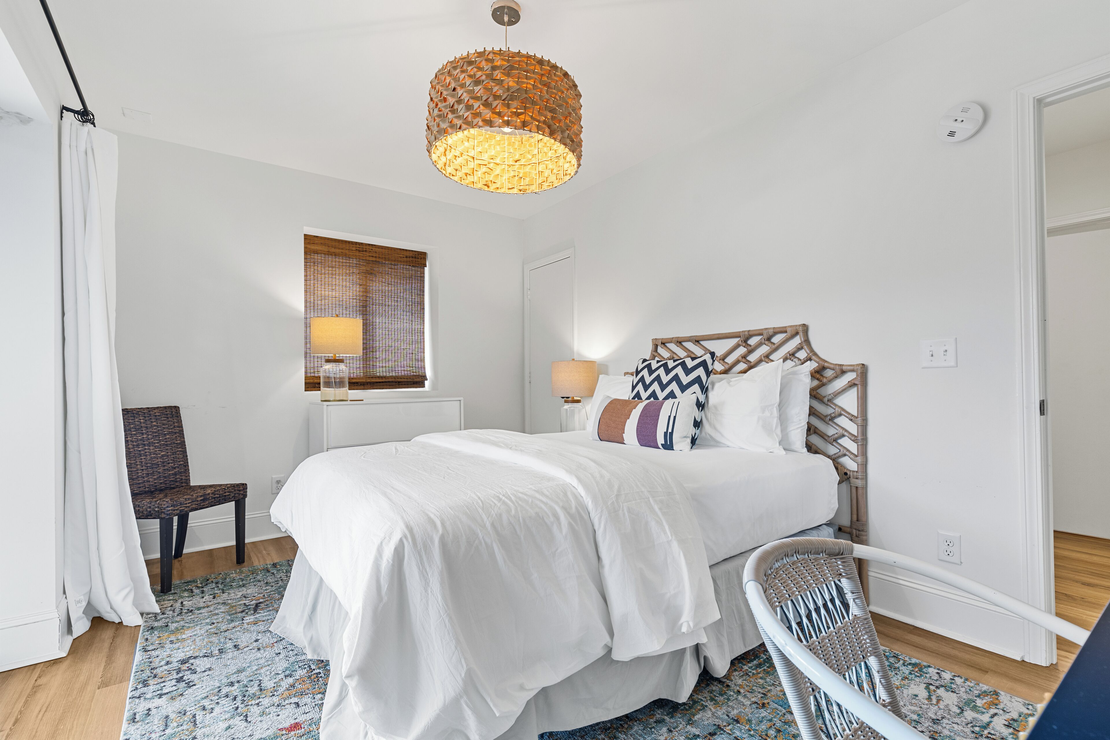 Ein Schlafzimmer mit Bett, Stuhl, Lampe und einem Fenster mit Jalousien.