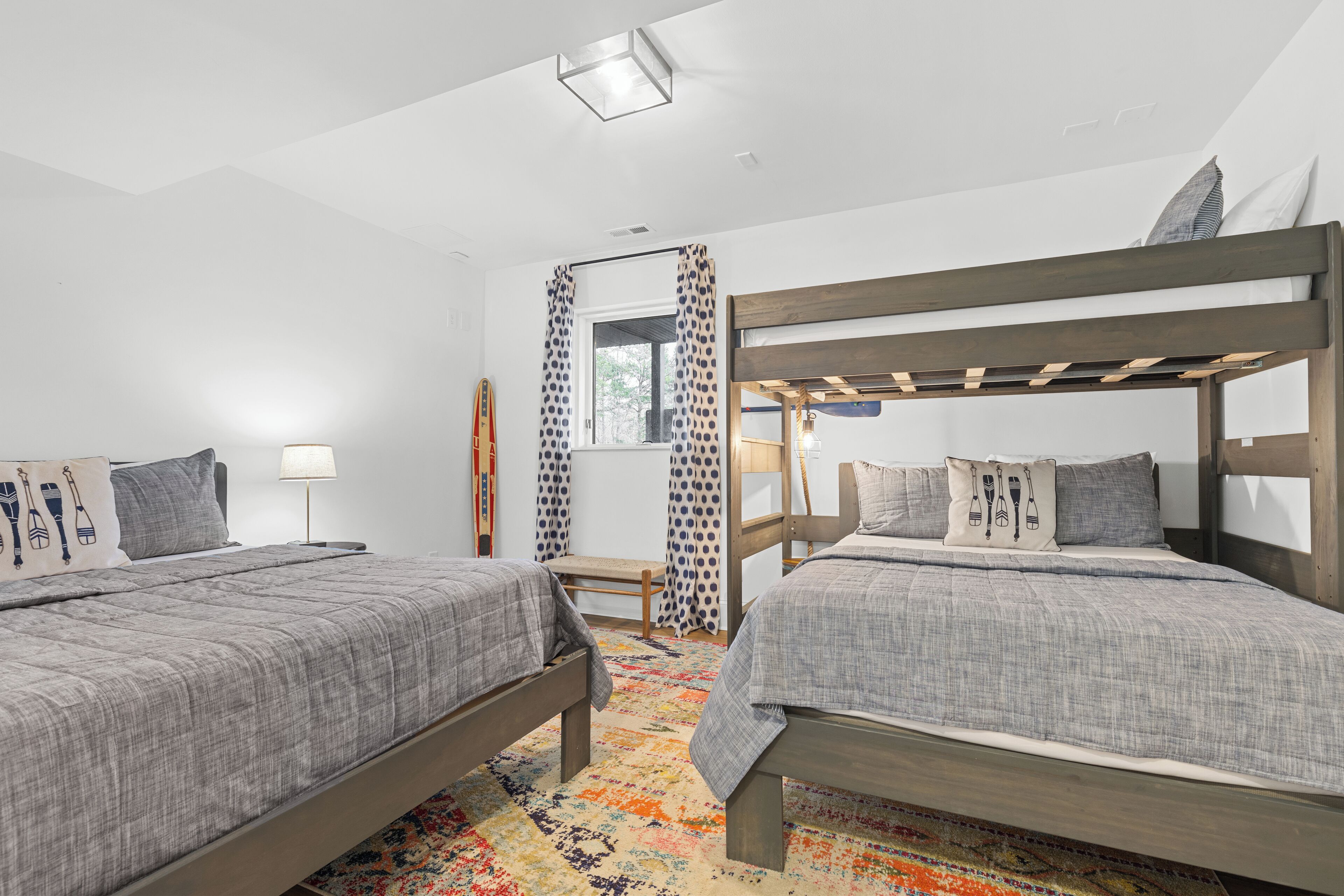 Une chambre avec deux lits, une fenêtre avec des rideaux, un bureau et un tapis coloré.