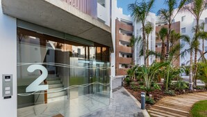 A modern building with a glass entrance, a visible number '2' on the glass, and a surrounding garden with palm trees and a wooden deck. - Ref. 502550 (Motril)