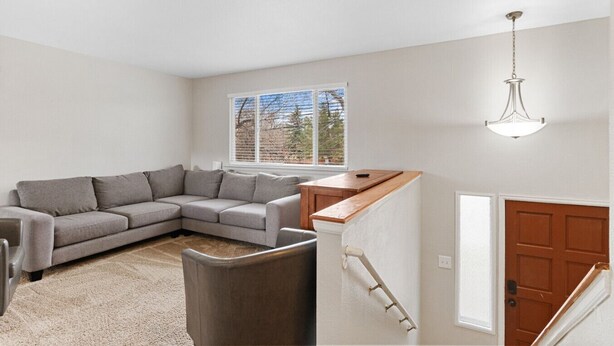 A living room with a grey sectional sofa, a small wooden table, a trash can, and a staircase leading to a door. - All New Sleeps 6/Old Town Arvada (Arvada)
