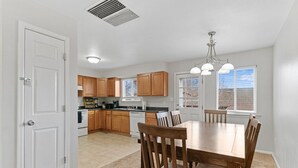 A kitchen with wooden cabinets, a dining table with chairs, and a window with blinds. - All New Sleeps 6/Old Town Arvada (Arvada)