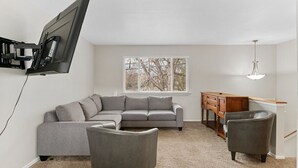 A living room with a grey sectional sofa, two armchairs, a wooden sideboard, and a TV mounted on the wall. - All New Sleeps 6/Old Town Arvada (Arvada)