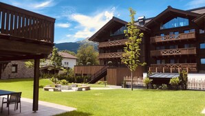 A modern building with a wooden facade, large windows, and a balcony overlooking a grassy area. - Beautiful Chalet With Swimming Pool (Ehrwald)