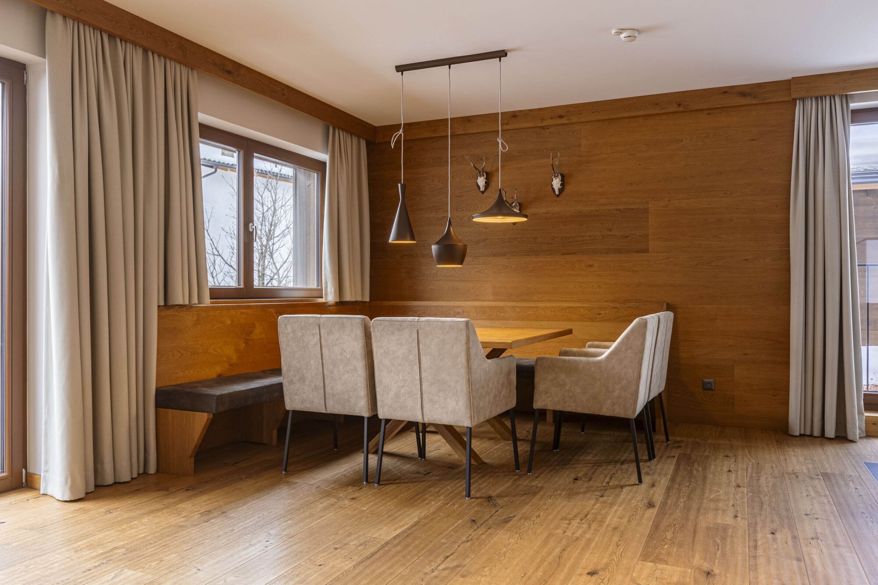 Un espace repas comprenant une table et des chaises en bois, un banc et des luminaires suspendus.
