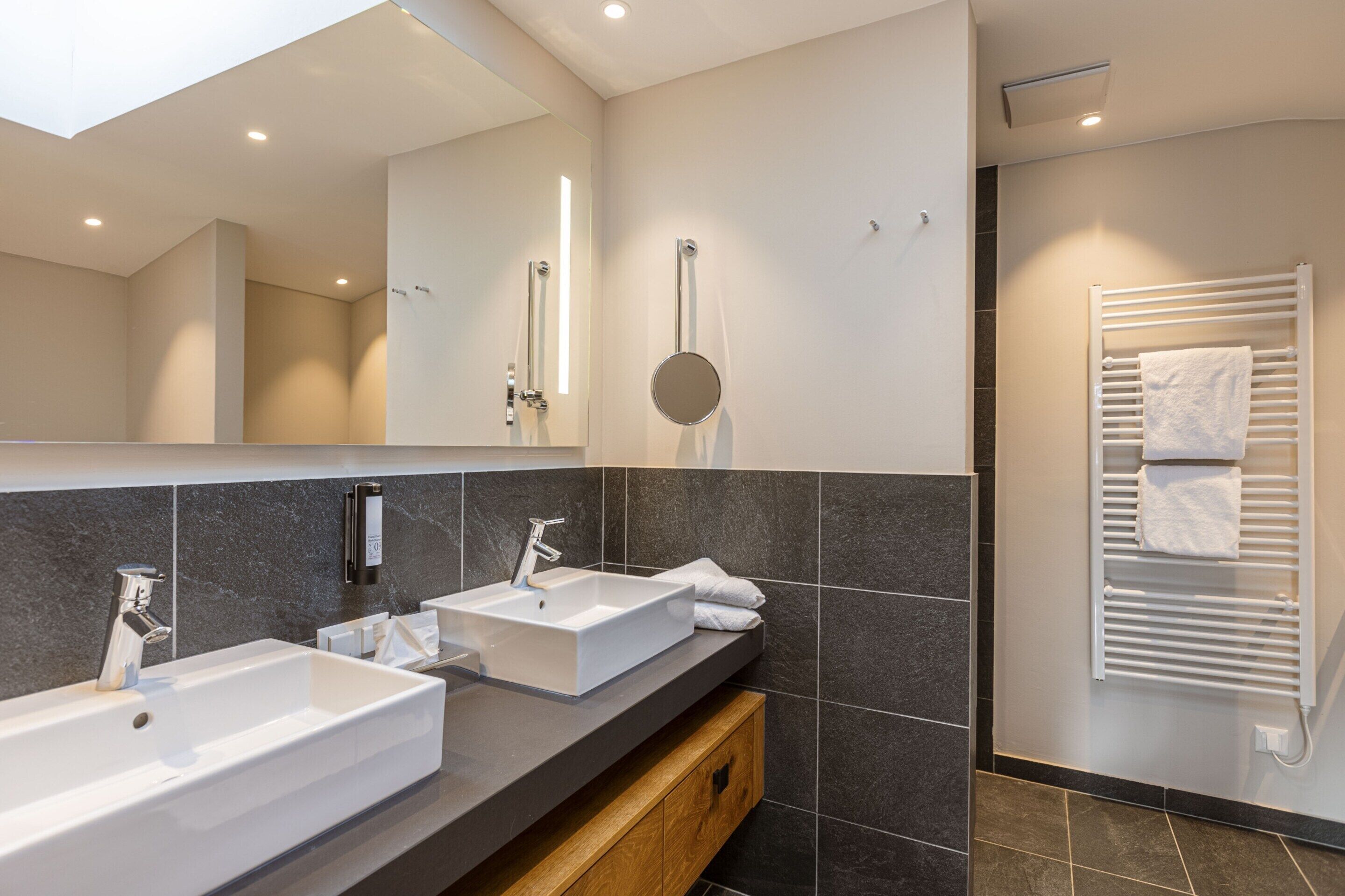 Un bagno moderno con due lavabi, uno specchio, un portasciugamani e un termosifone per asciugamani.