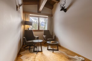 Habitació acollidora amb dues butaques de cuir, una taula rodona petita, un feser de llana i una finestra amb vista a la muntanya.