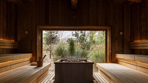 A sauna with wooden benches and a central heating element, surrounded by wooden walls and a view of trees. - Beautiful Chalet With Swimming Pool (Ehrwald)