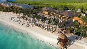 Un complexe hôtelier comprenant plusieurs bâtiments de style bungalow, une plage avec des chaises longues et un espace piscine.