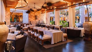 Un restaurant doté de nombreuses tables, de chaises en osier et d’un mur en pierre servant de décor.