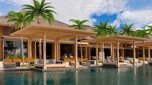 Un espace aménagé au bord de la piscine, avec des chaises longues et un coin salon abrité, le tout entouré de palmiers.