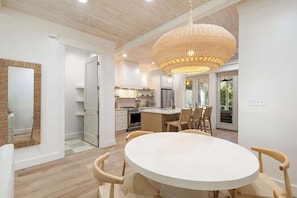 Una cocina moderna con armarios blancos, un comedor con una mesa redonda y sillas, y una lámpara colgante grande de fibras naturales.