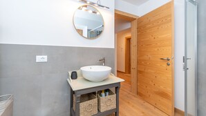 A modern bathroom with a round mirror, a white sink, and a wooden door.
