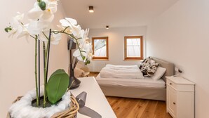Een slaapkamer met een bed, nachtkastje, lamp en een orchidee.