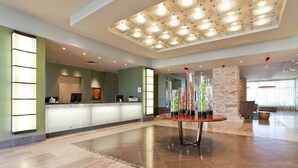 Un hall d’hôtel comprenant un comptoir d’accueil, une table décorative en verre agrémentée de vases et un design de plafond moderne.