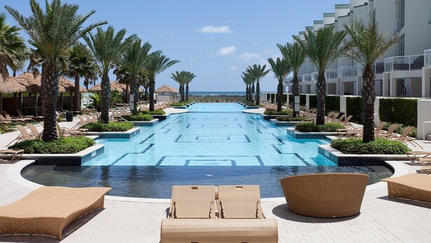 Une piscine entourée de chaises longues et de palmiers, le tout adossé à un bâtiment moderne.