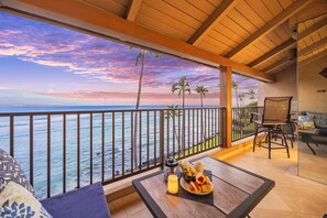 Een balkon met uitzicht op de oceaan, een tafel met eten en drinken, en een zithoek met stoelen en een bank.