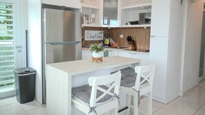 A modern kitchen with a stainless steel refrigerator, white cabinetry, and a small dining table with checkered chairs. - Spacious and Modern Beach House With Pool (Hatillo)