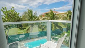 A balcony with a glass railing, two white lounge chairs, and a swimming pool. - Spacious and Modern Beach House With Pool (Hatillo)