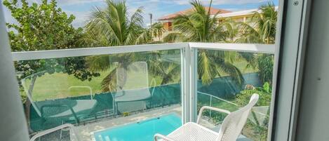 Un balcon doté d’une rambarde en verre, deux fauteuils de jardin blancs et une piscine.