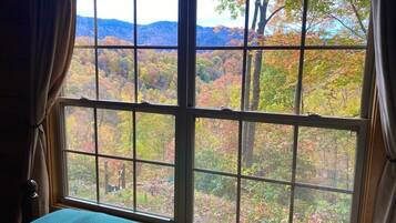 A room with a large window offering a view of a forested area with autumn foliage.