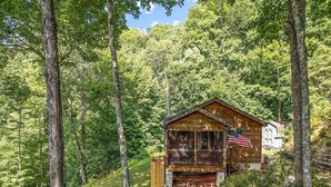 Una cabaña de madera con porche, rodeada de un bosque denso.