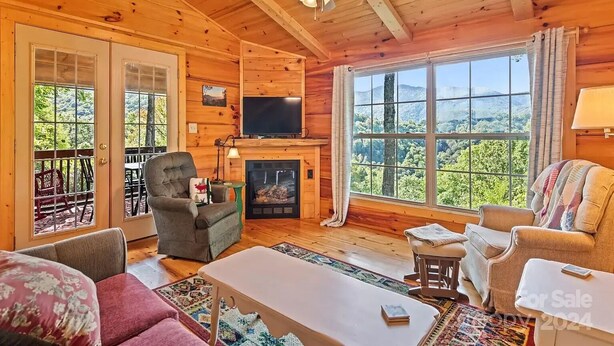 Interior acogedor de una cabaña con chimenea, paredes de madera, un televisor y un ventanal con vistas panorámicas.