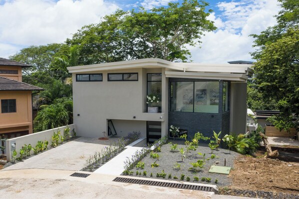 A modern two-story house with a flat roof, large windows, and a small balcony.