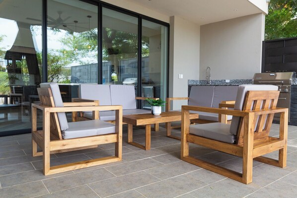 An outdoor patio with wooden furniture and a glass door leading to a kitchen area.