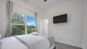 A bedroom with a large bed, a TV mounted on the wall, and a window with curtains.