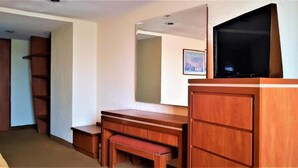Une chambre d’hôtel avec un bureau en bois, un téléviseur posé dessus, un banc et une armoire.