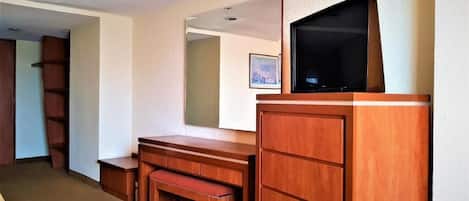Ein Hotelzimmer mit einem Holztisch, einem Fernseher darauf, einer Bank und einem Kleiderschrank.
