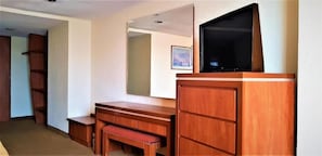Een hotelkamer met een houten bureau, een televisie erboven, een bankje en een kledingkast.