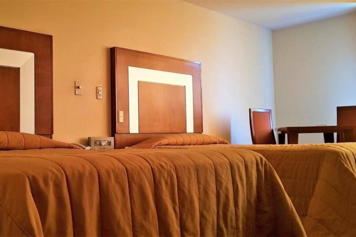 Une chambre d’hôtel avec deux lits, des têtes de lit en bois et une petite table avec une chaise.