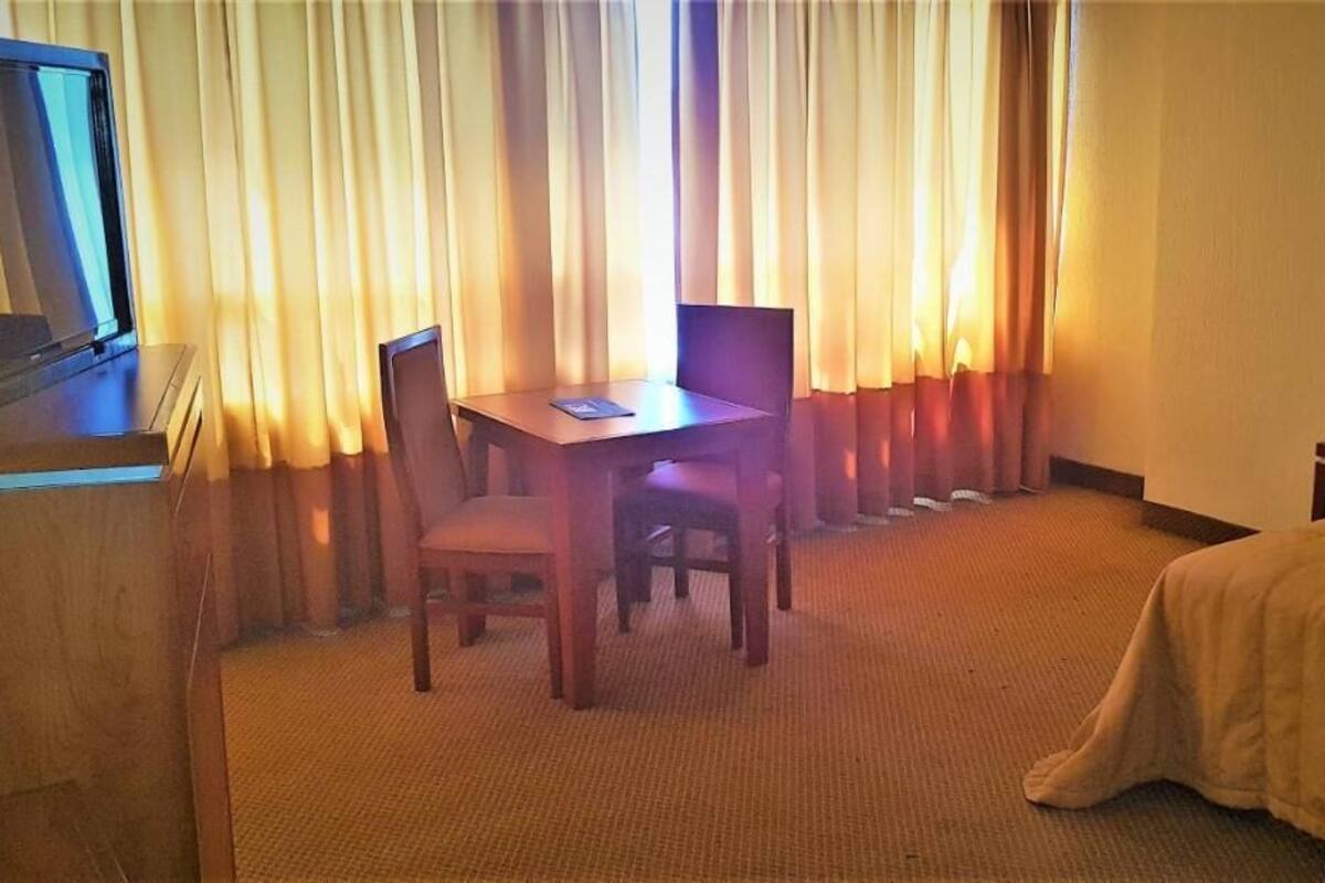 Une chambre d’hôtel avec un lit, un bureau et une chaise, une télévision et des rideaux.