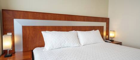 A hotel room with a wooden headboard, a white bedspread, two pillows, a bedside lamp, and a telephone on the nightstand.