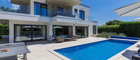 A modern two-story house with a swimming pool, outdoor seating, and a table tennis table.