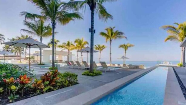 A swimming pool with lounge chairs and palm trees, surrounded by a landscaped area.