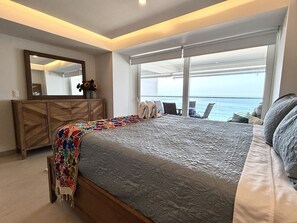 Een slaapkamer met een bed, een kaptafel, een spiegel en uitzicht op zee.
