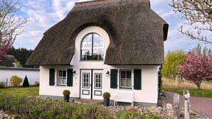 A house with a thatched roof, white walls, and green shutters.