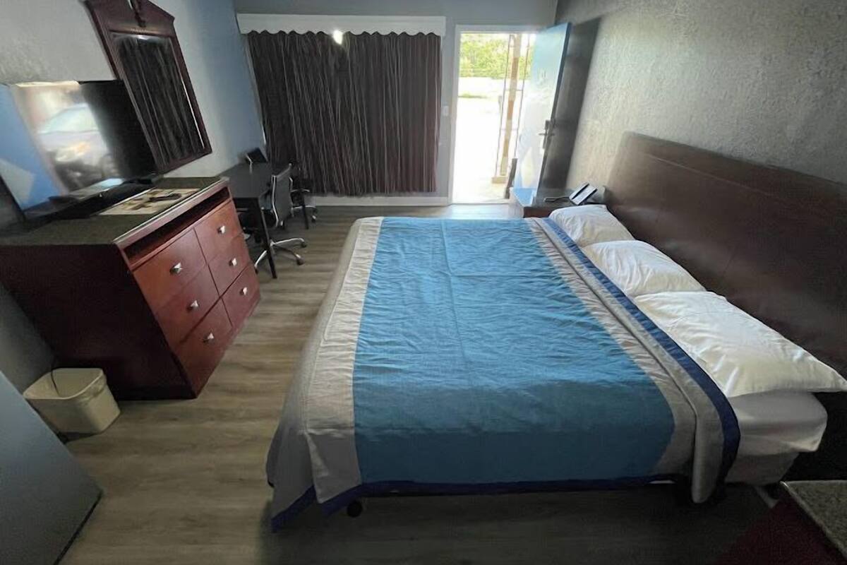 A hotel room with a bed, a desk with a chair, a dresser, and a television.