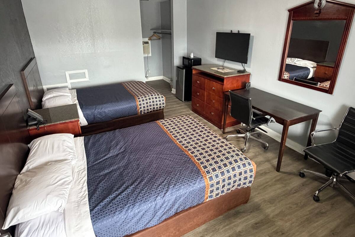 A hotel room with two beds, a desk, a chair, a TV, and a mirror.