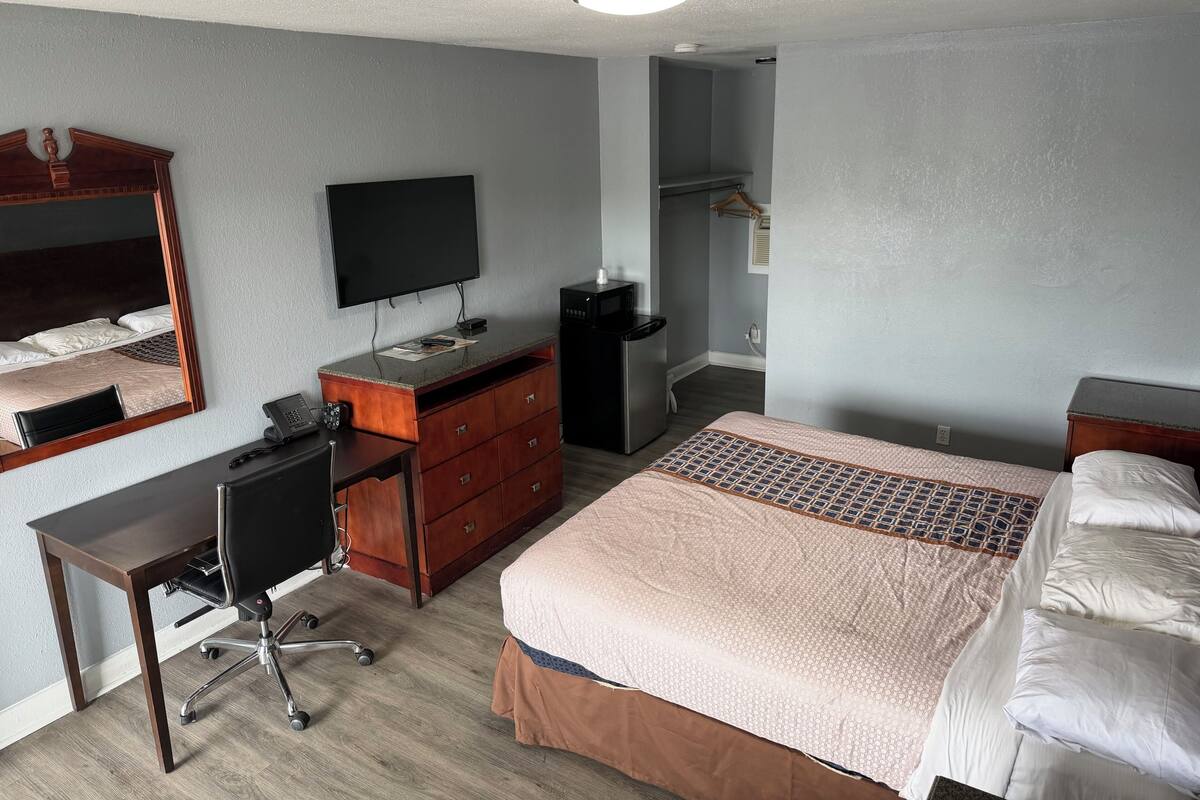 A hotel room with a bed, a desk, a dresser, a television, and a microwave.
